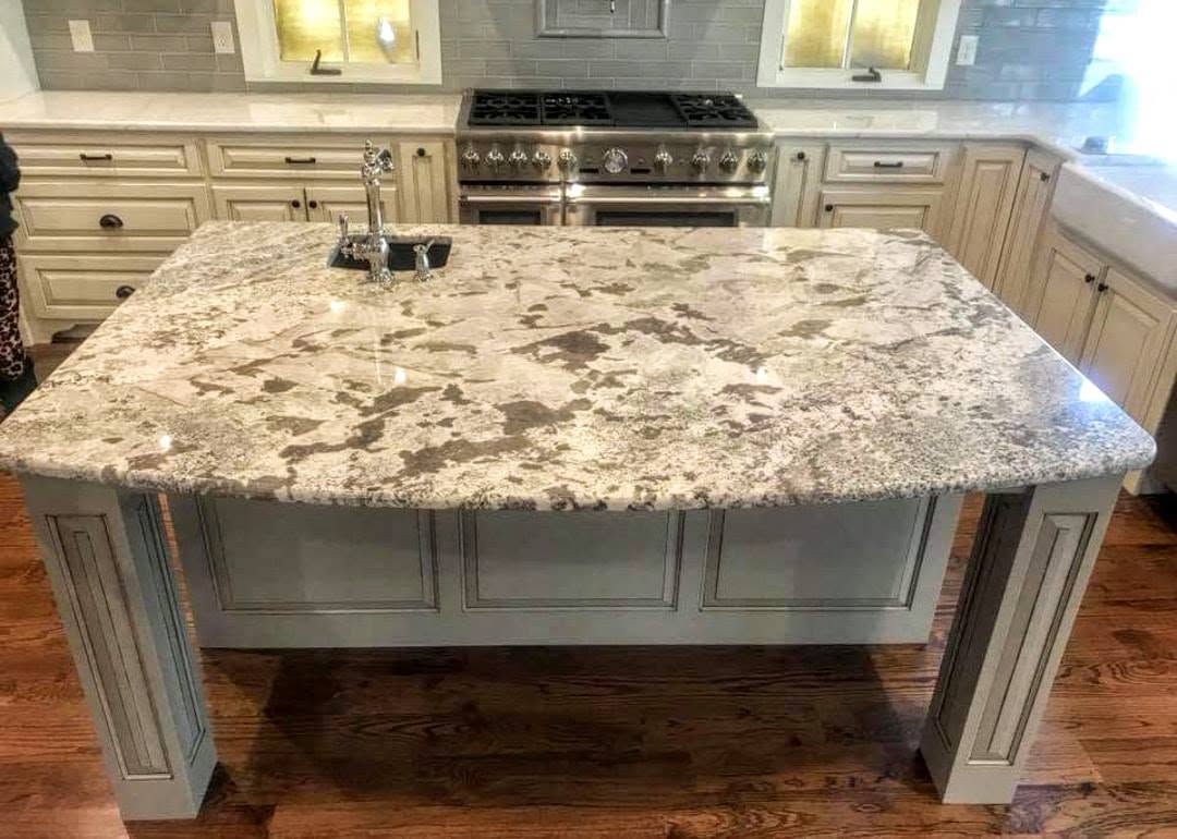 Kitchen island topped with heavily veined natural granite beside painted cabinetry