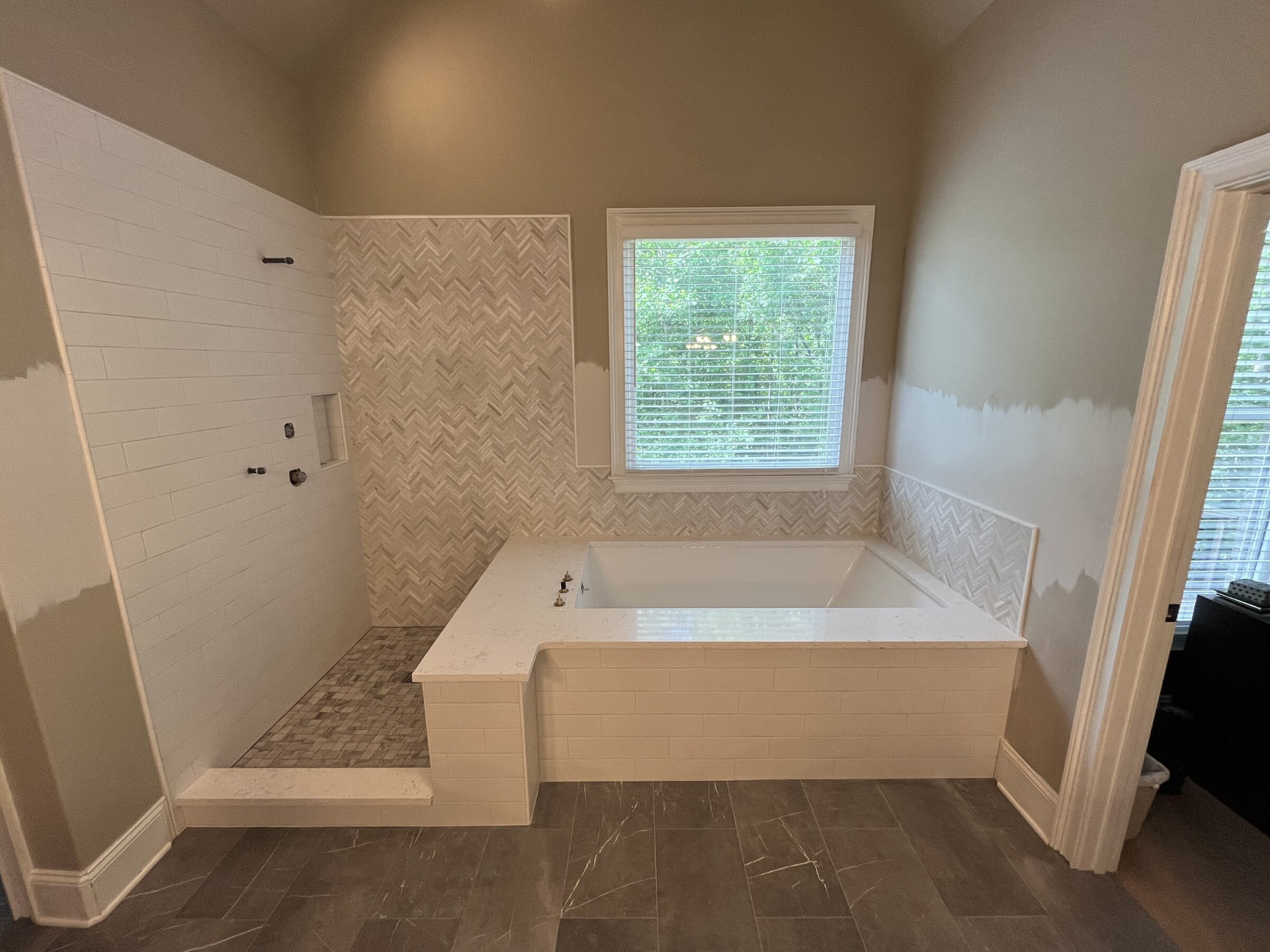 White stone tub deck beside a walk-in shower with herringbone tile