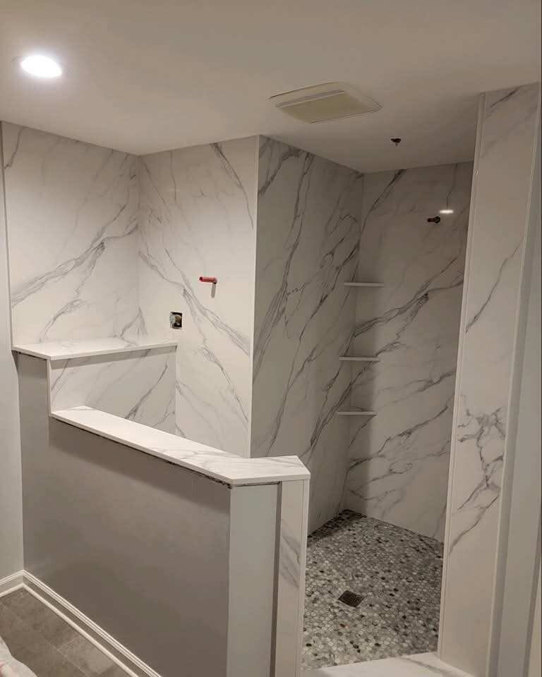 Walk-in bathroom shower with full-height marble-look wall panels, a recessed shelf, and stone curb