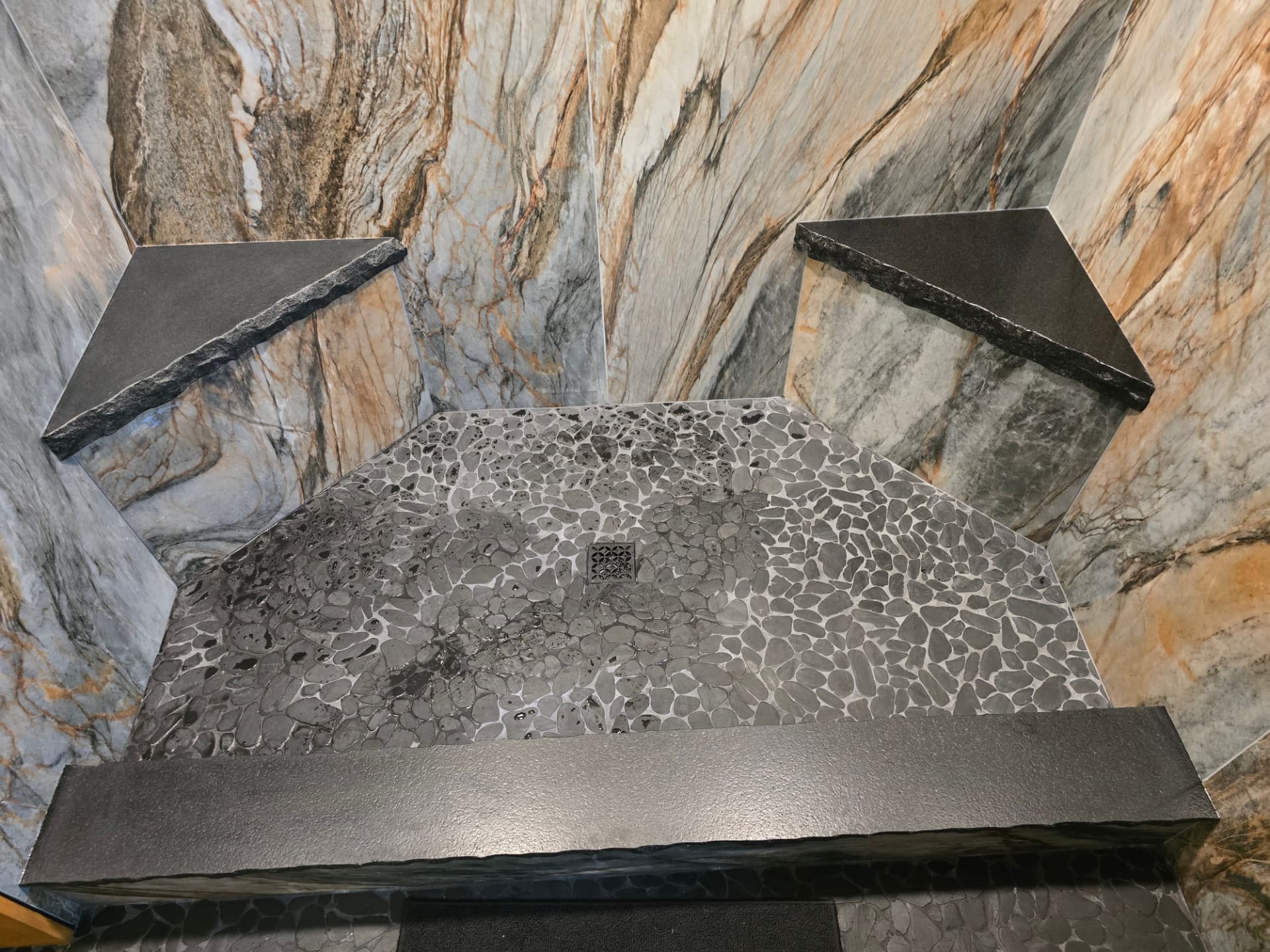 Custom stone shower with full-height wall slabs, corner benches, and a pebble floor
